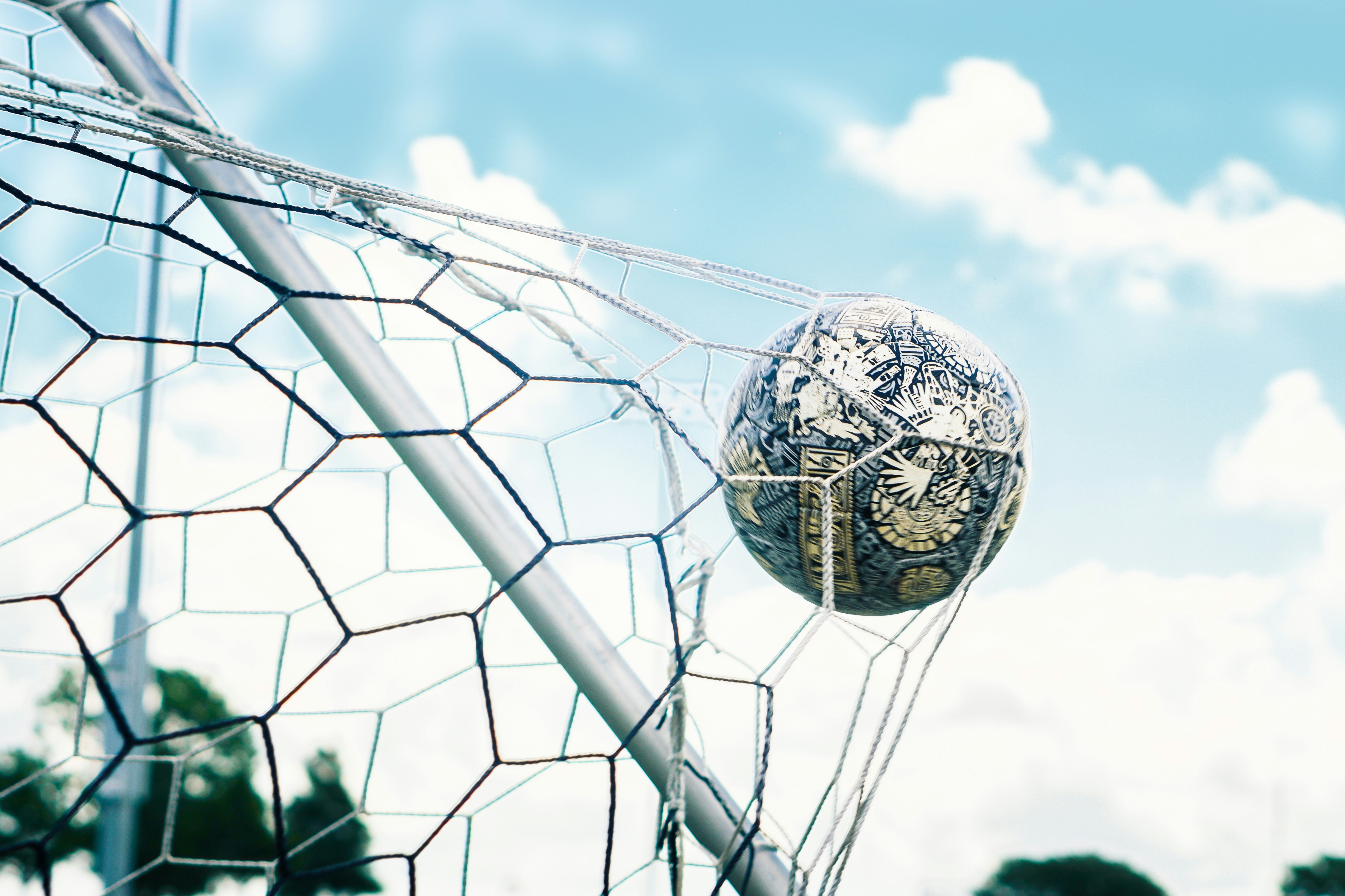 A soccer ball scoring a goal in a net against a blue sky.