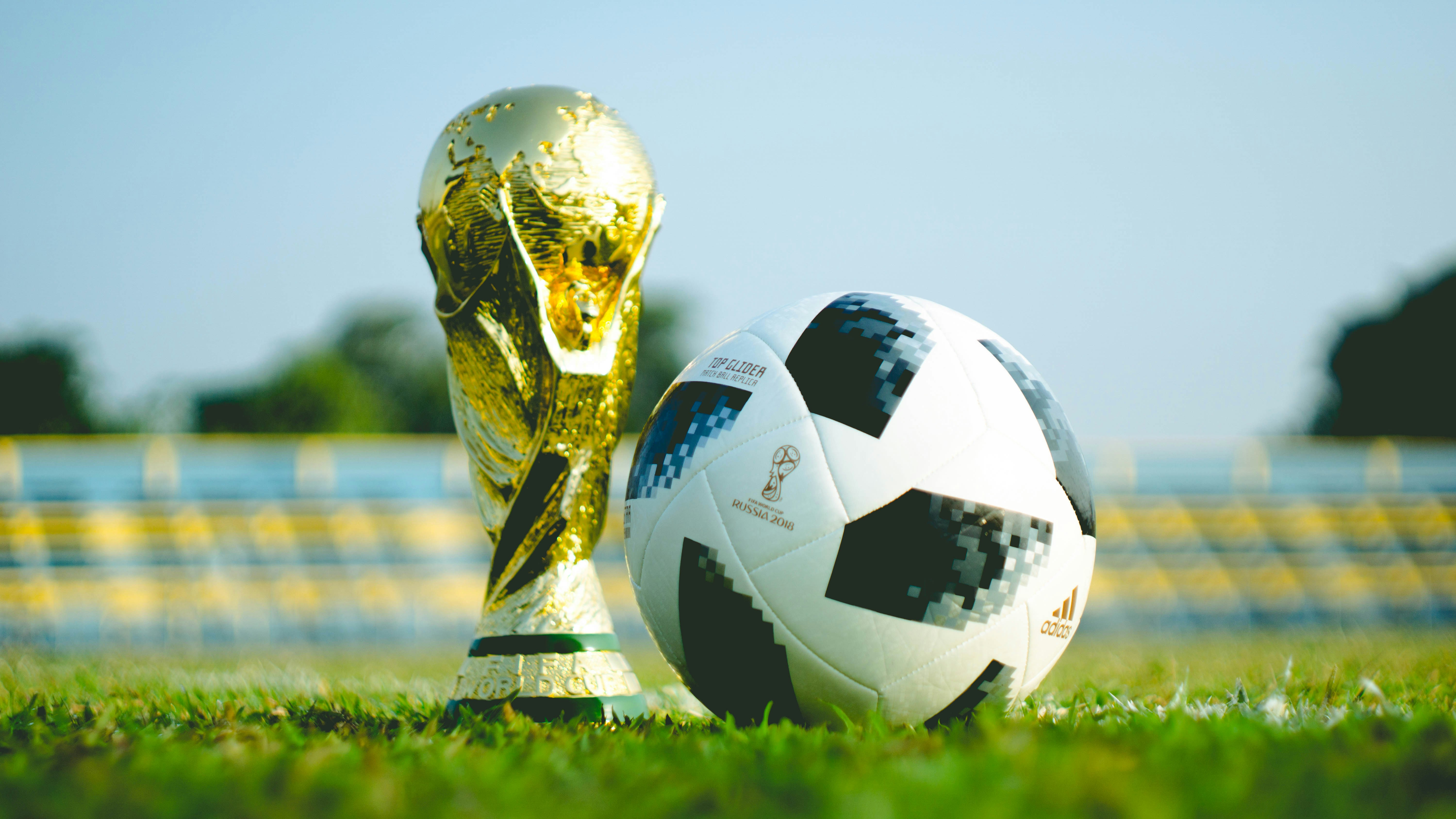 The FIFA World Cup trophy standing next to a soccer ball on a green pitch.